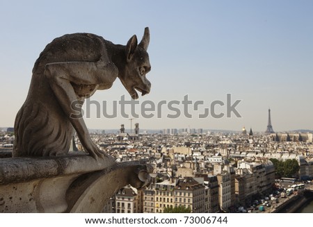 Stone gargoyle with horns peering over the city of Paris towards the Eiffel Tower while perched on a corner of the cathedral of Notre Dame.