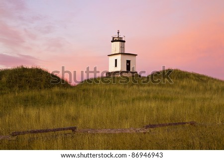 As the dawn sun comes up over the horizon, the lighthouse at Cattle Point on San Juan Island lights up as the sky behind glows with pink and magenta colors.