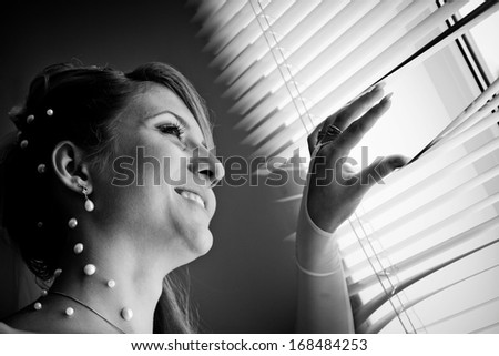 Stylized black and white photo ofl bride waits for groom near the window.