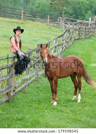 Man in cowboy clothes sitting on the fence beside the horse