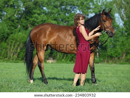 Young red haired horsewoman leading horse through grassy field