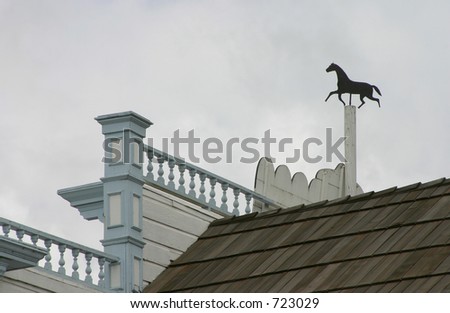 A wind vane in the shape of a horse, on top of an old stables.