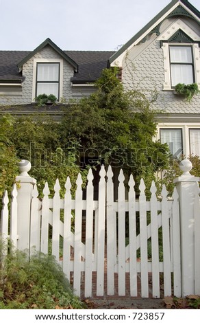 Picket fence entry gate leads to an overgrown front yard of an old house.