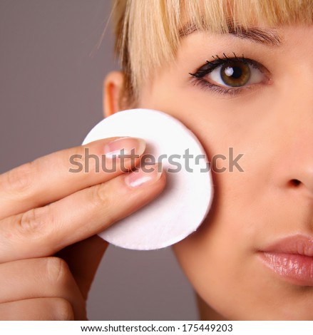 Woman removing face makeup with cotton pad - skin care concept. Facial closeup, young woman isolated on grey background.