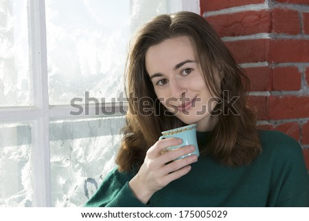 Young woman with a cup of tea by the winter window