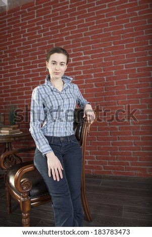 Girl in a blue shirt and jeans to leather chair against a background of red brick wall