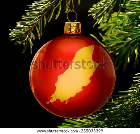 A red bauble with the golden shape of  Isle of Man hanging on a christmas tree isolated on black.(series)