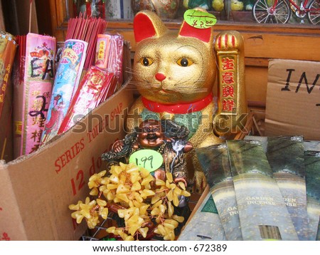 A golden Chinese cat for sale sits among a Buddha statue and incense sticks.