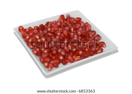 Closeup of bright red pomegranate seeds displayed in a square white dish.
