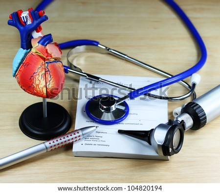 A doctorÃ¢Â?Â?s desk showing a purple stethoscope, resting on a sick certificate pad with the other diagnostic doctors tools  and a detailed model of the human heart.