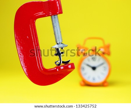 A silver Pound symbol placed in a red clamp with a yellow background, with an orange alarm clock in the background indicating the pressure on the pound sterling.