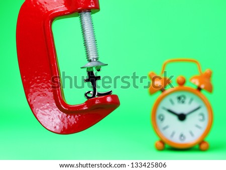 A silver Pound symbol placed in a red clamp with a pastel green background, with an orange alarm clock in the background indicating the pressure on the pound sterling.