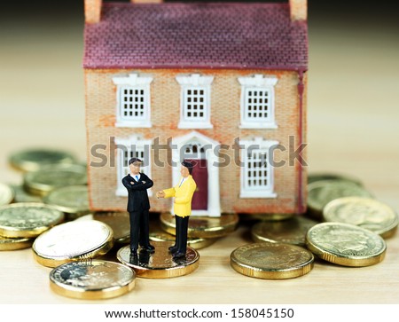 A real estate agent and a prospective buyer in front of a house resting on gold coins, with the prospective buyer not impressed with very negative body language, suggesting you can\'t win them all!