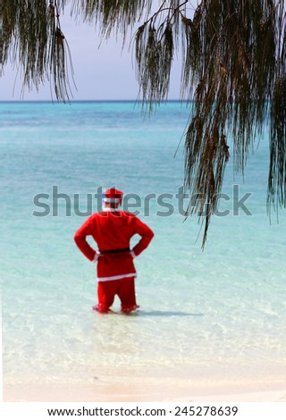 Father Christmas on Boxing Day, relaxing on a tropical island in the ocean still in his Father Christmas suit, celebrating the end of a long night