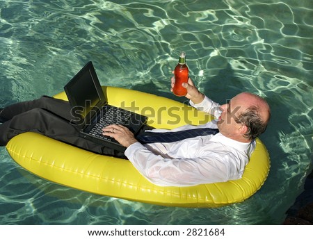 Businessman in suit and tie in a swimming pool with laptop and a beer in one hand floating in an inflatable boat and using his laptop