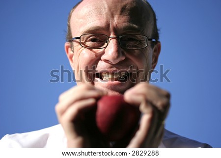 Doctor holding juicy red apple in both hands and smiling, showing head, hands, apple , doctors laboratory coat and a beautiful blue sky in the background