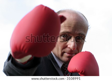 Businessman in suit wearing boxing gloves to protect him from the angry shareholders