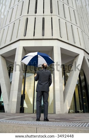 Businessman with umbrella open and his back to the camera on the steps, about to go to his next appointment with the tall building in front of him
