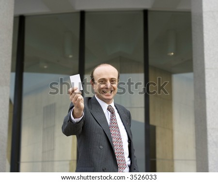 Businessman wearing business attire holding up a business card towards you, with a beautiful blue sky behind