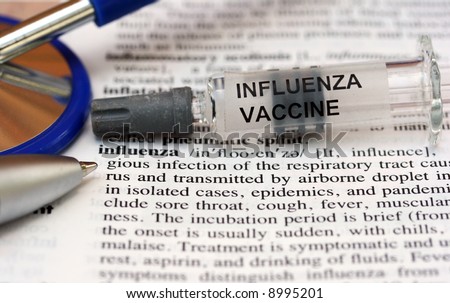A syringe containing the influenza vaccine laid on a doctors medical dictionary open at the influenza page.