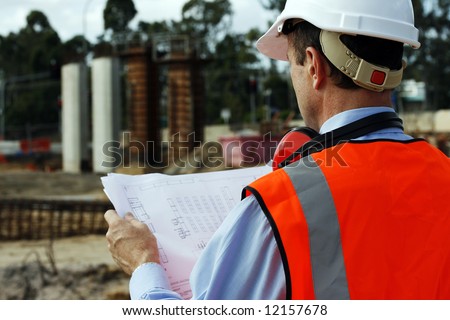 Engineer on the construction site looking at the plans, wearing white safety helmet and reflective vest