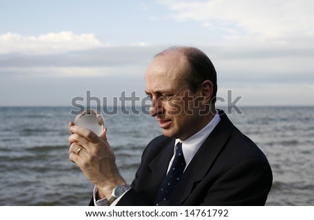 Man holding a crystal globe of the earth in his hands with the ocean in the back ground.
