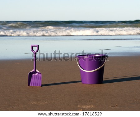 A purple plastic bucket and spade on the beach with the ocean behind coming in