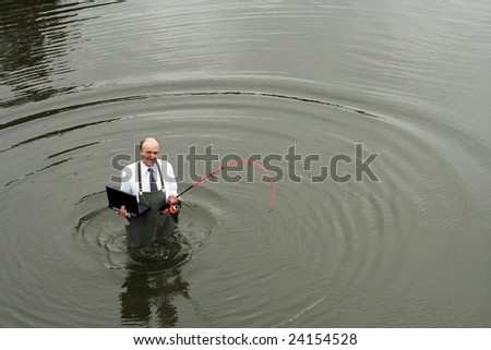 A well businessman in a river in waders with a fishing rod in one hand and a laptop in the other, trying to achieve a working balance with his social life.