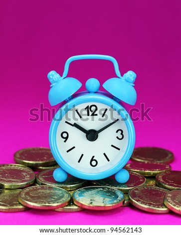 A light blue alarm clock placed on some golden coins with a purple back ground, asking the question how long before your investment matures?