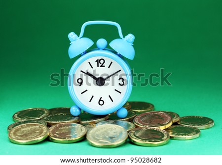 A light blue alarm clock placed on some golden coins with a green back ground, asking the question how long before your investment matures?