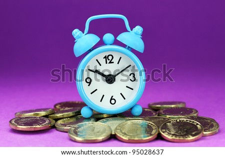 A light blue alarm clock placed on some golden coins with a purple back ground, asking the question how long before your investment matures?