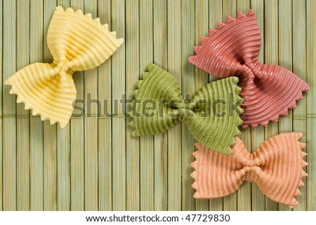 Several multi-colored pasta laid on a straw mat.