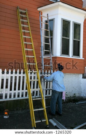 man adjusting ladder painting outside of house