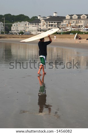 boy carrying surfboard on head on beach