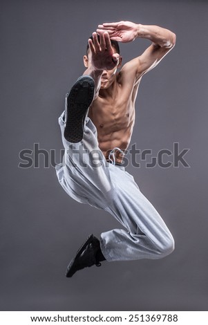 Young asian man workout over grey background karate jump kick