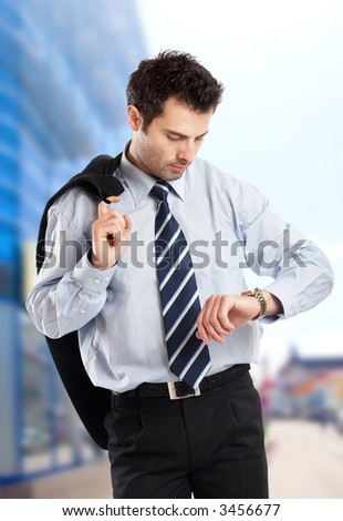 Busy businessman with jacket on his shoulder looking at his watch in front of a glass building - check my portfolio for similar photos