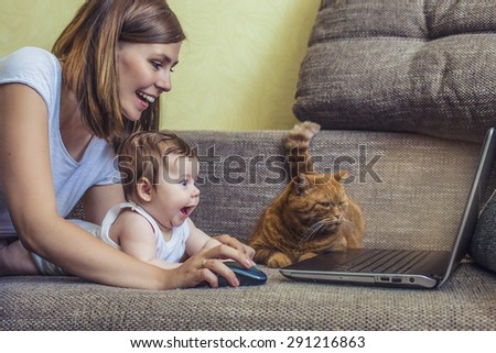 The woman with a baby and a cat at the laptop lying on the couch