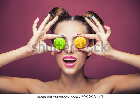 Model, a woman with bright make-up and colour biscuits joking. Studio, beauty, glitter, sweets.
