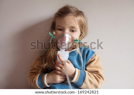 Little blond girl holding the mask for inhalation