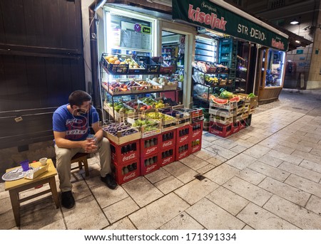 SARAJEVO, BOSNIA AND HERZEGOVINA - AUGUST 13, 2012: Salesman sits in front of the street grocery shop at night.