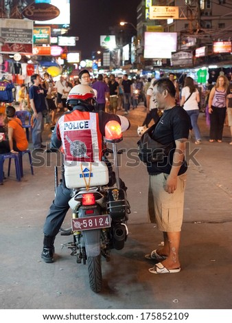 BANGKOK, THAILAND - JANUARY 9, 2012: Local man talks on the street with policeman on the motorcycle on Khao San Road. Royal Thai Police counts about 230,000 officers.