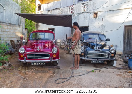 UNAWATUNA, SRI LANKA - MARCH 6, 2014: Local man washing two Morris Minor cars in the yard with water hose. There are estimated to be as many as 4,000 Minors still on the road in Sri Lanka.