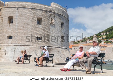 DUBROVNIK, CROATIA - MAY 27, 2014: Elderly couple  sitting on bench on dock in front of the St. John fortress near the old port. Fortress houses the Maritime Museum and the aquarium.