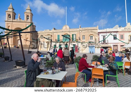 MARSAXLOKK, MALTA - JANUARY 11, 2015: People eating at restaurant terrace in front of the Parish Church of Our Lady of Pompei.
