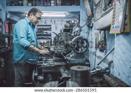 JODHPUR, INDIA - 17 FEBRUARY 2015: Mechanic working late in workshop with scattered equipment and machinery. Post-processed with grain and texture.
