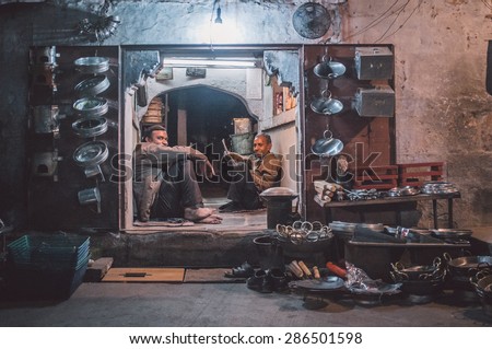 JODHPUR, INDIA - 16 FEBRUARY 2015: Two workers sit and rest before closing time. Stores with kitchen pottery made from metal are common on Asian markets. Post-processed with grain and texture.