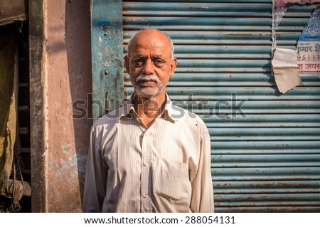 VARANASI, INDIA - 20 FEBRUARY 2015: Elderly Indian man with white beard  stands in street next to closed store. - Stock Image - Everypixel