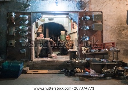 JODHPUR, INDIA - 16 FEBRUARY 2015: Two workers sit and rest before closing time. Stores with kitchen pottery and other products made from metal are common on Asian markets.