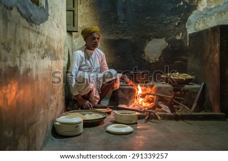 GODWAR REGION, INDIA - 12 FEBRUARY 2015: Indian man dressed in traditional clothes makes chapati on open fire in old kitchen. Chapati is an unleavened flatbread.