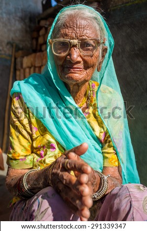 GODWAR REGION, INDIA - 13 FEBRUARY 2015: Elderly Indian woman in sari with covered head and repaired glasses sits in doorway of home.